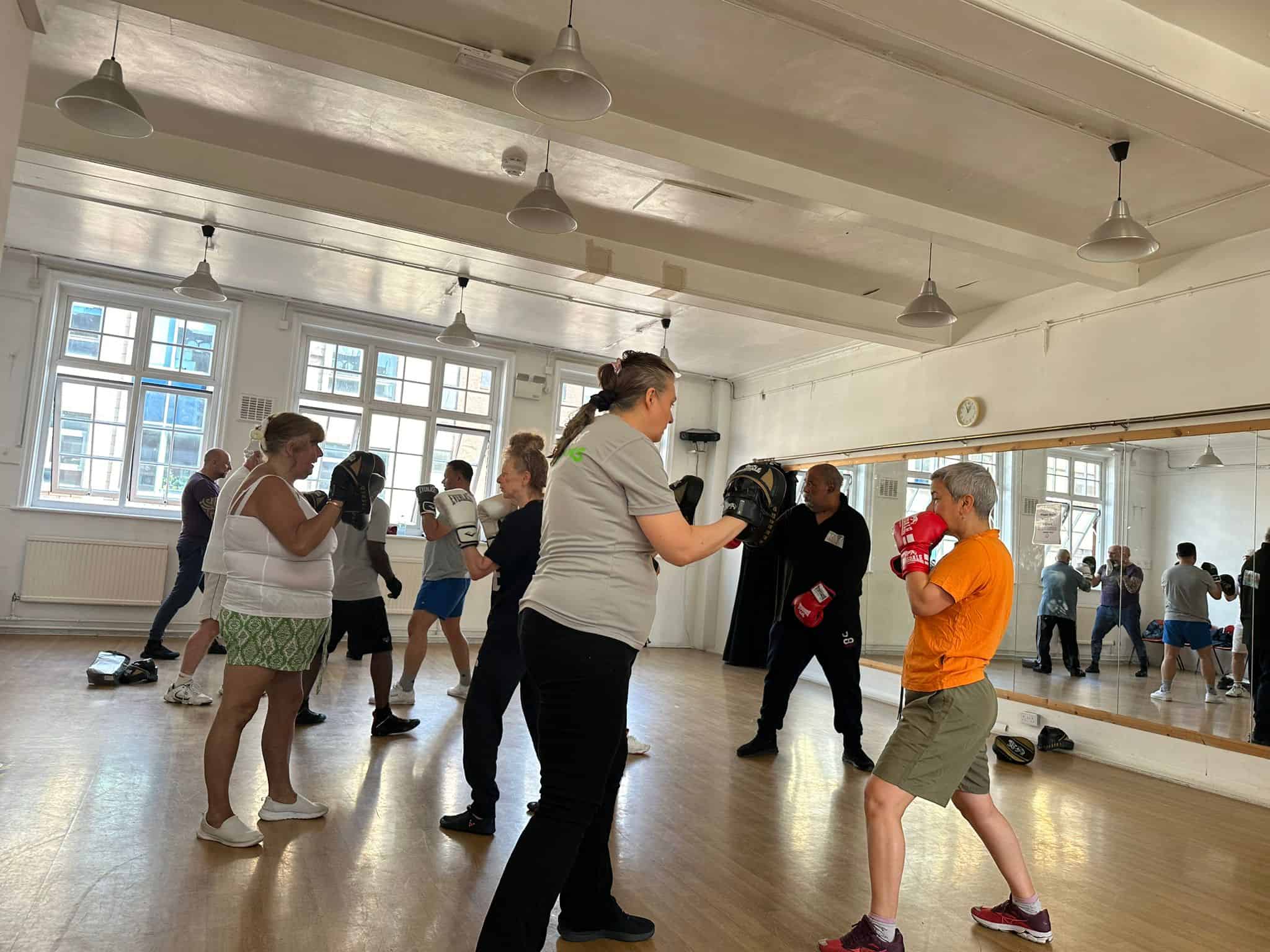 Protective boxing training session with diverse participants in a bright, spacious gym.