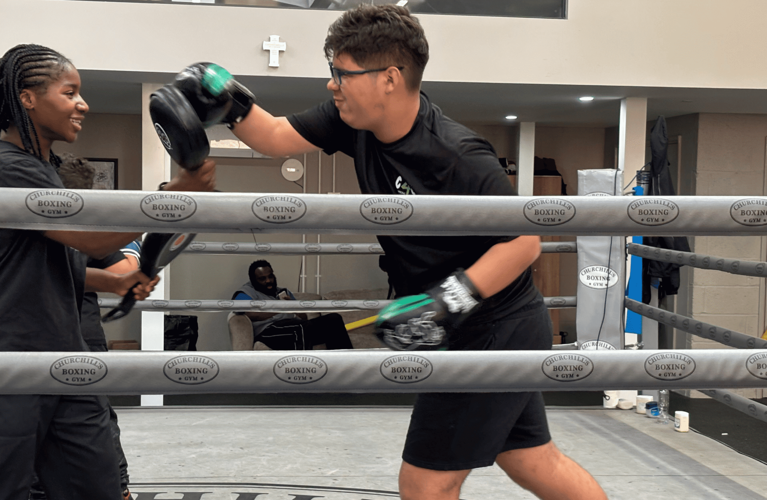 Young man practicing boxing with trainer in a gym boxing ring.