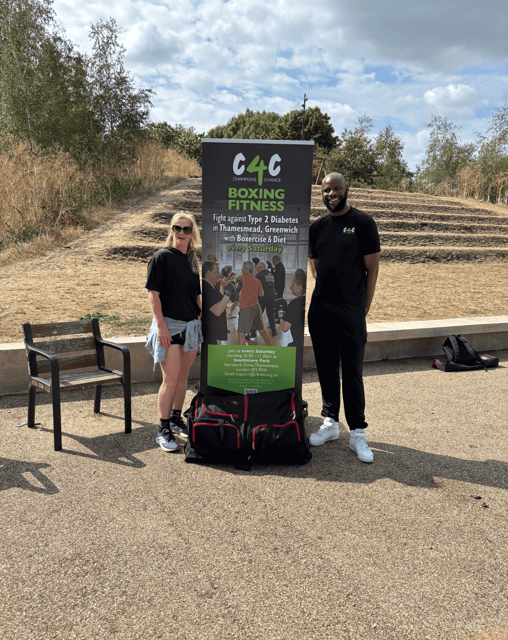 Two people standing outdoors next to a C4CWB fitness banner on a sunny day.