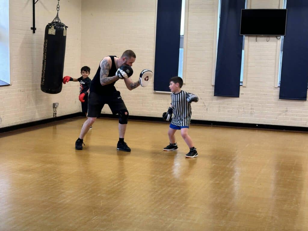 Young boy practicing boxing with coach in gym training session.