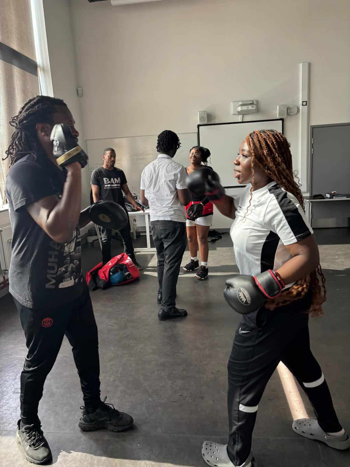 Women boxing training session in a modern gym with trainers and equipment.
