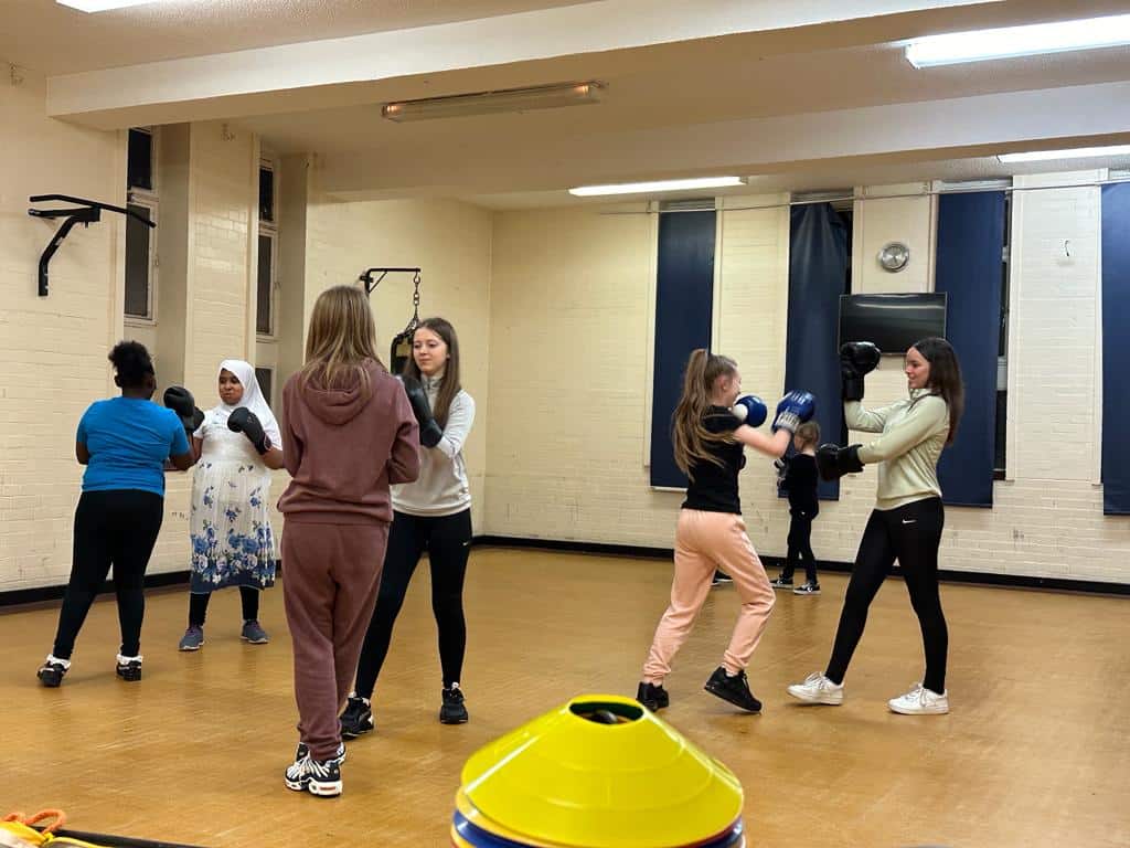 Boxing training session with women in a gym, practicing punches and techniques.