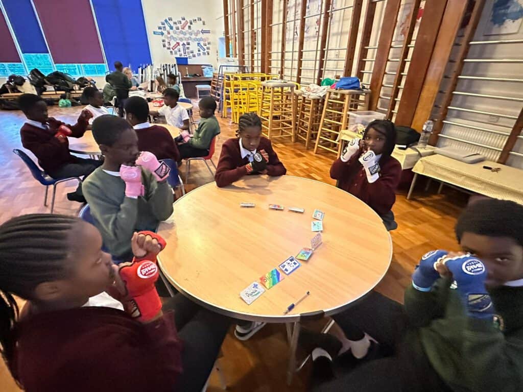 Playing card game with children in a school gymnasium, promoting social skills and fun activities.